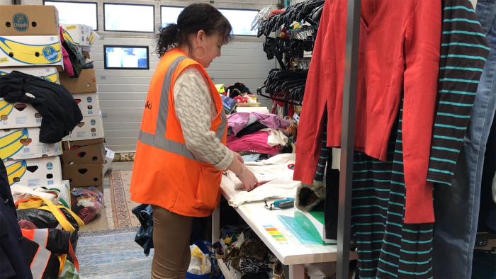 Nainen vaatteiden ja pahvilaatikoiden keskellä lajittelemassa tekstiilejä.