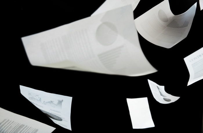 Valkoisia paperidokumentteja lentelee mustassa taustassa